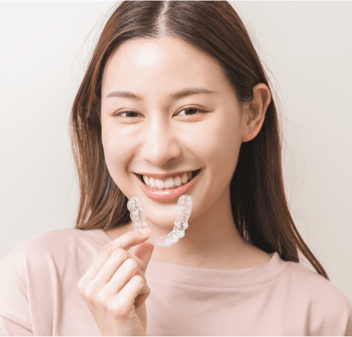 Woman smiling with nice teeth while holding clear aligner