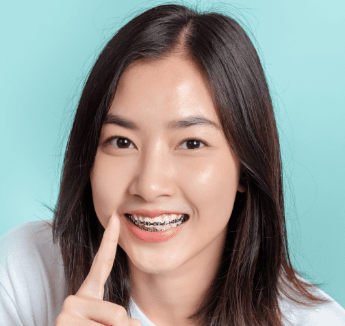 Woman with braces smiling while pointing at braces with blue background