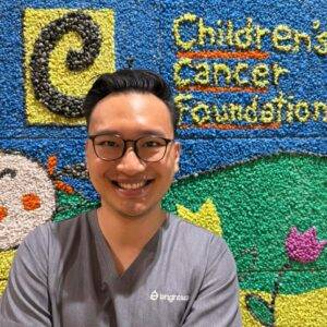 Doctor Jeremy smiling with background logo of Children's Cancer Foundation