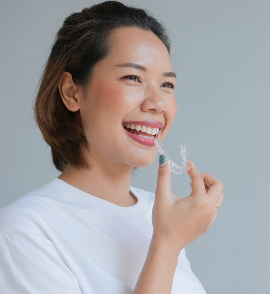 asian woman smiling with hand holding dental aligner retainer invisible