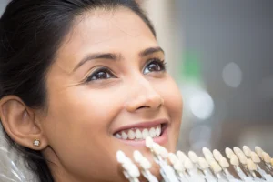 A dentist compares shade guide tabs against a patient's smile to select a natural-looking colour