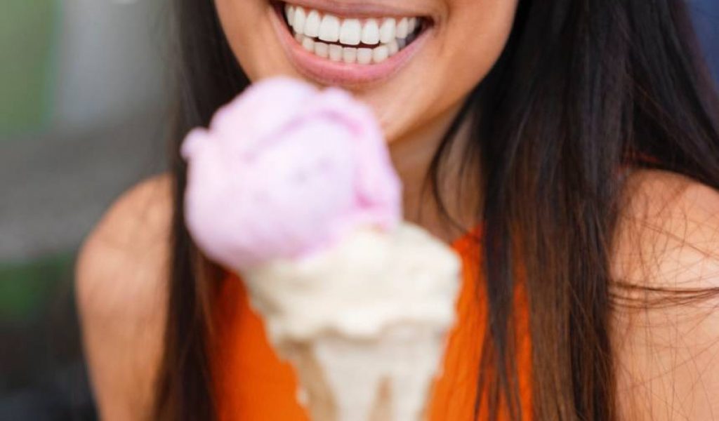 Woman smiling with white and neat teeth while holding out ice cream